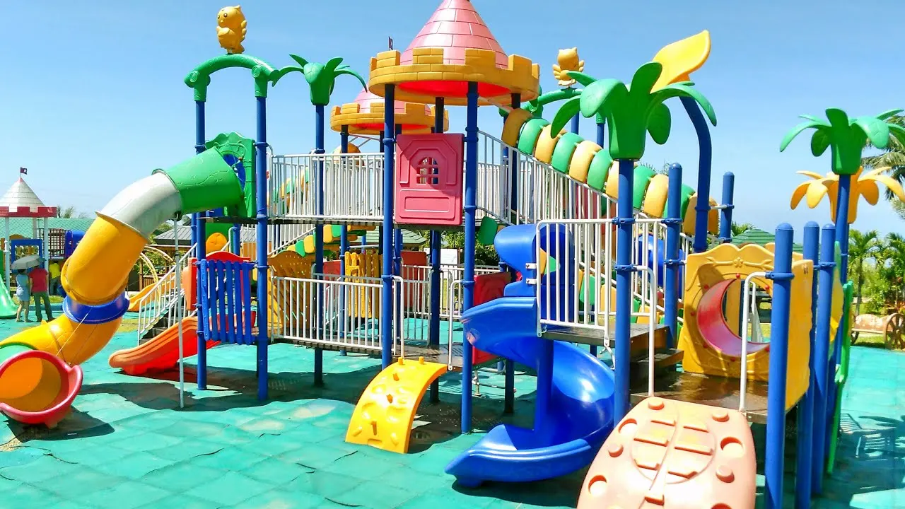 Parque infantil de exterior con torres tematizadas, palmeras, toboganes y suelo de caucho